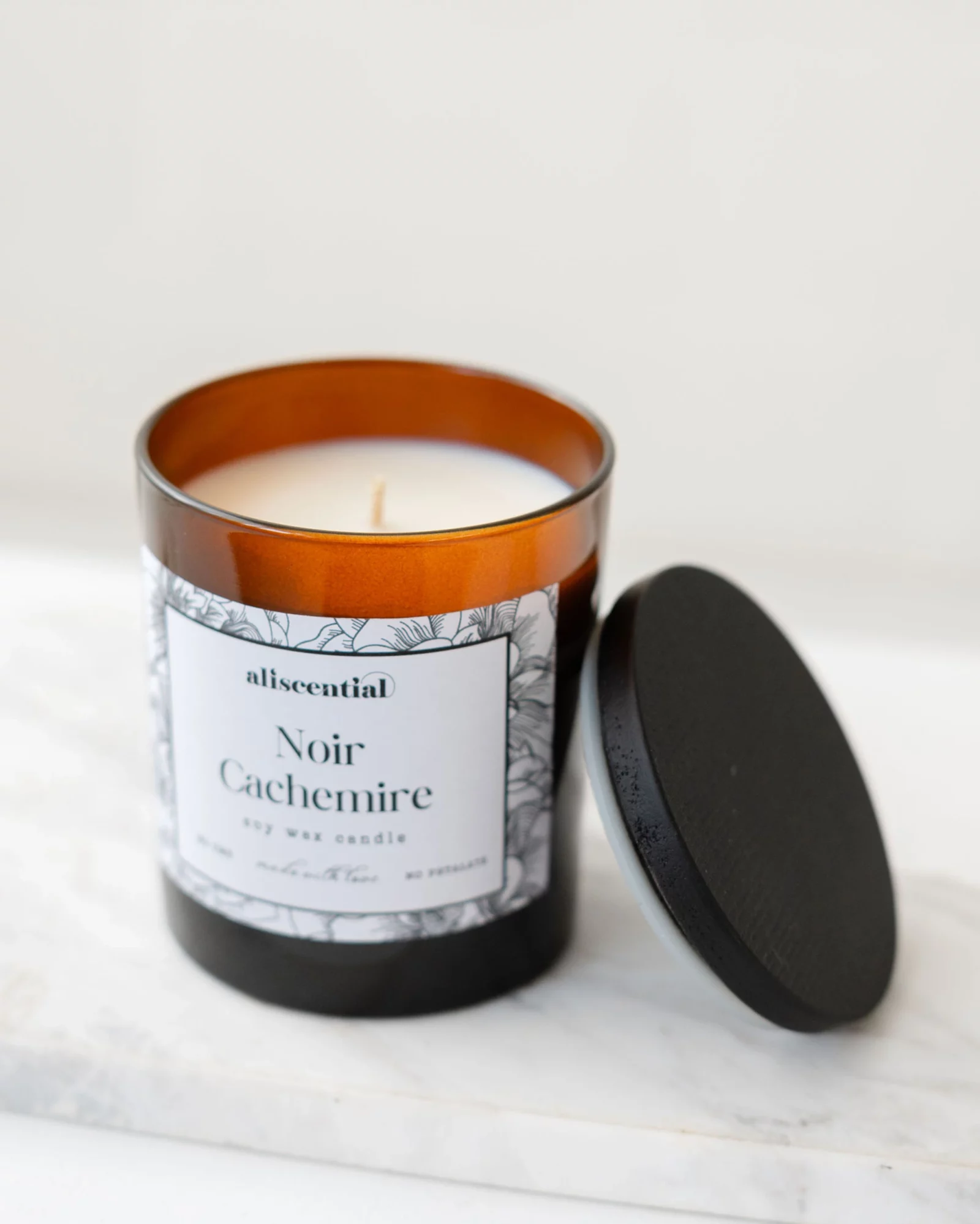 Bougie parfumée Noir Cachemire Aliscential en verre noir, packshot sur fond épuré. avec couvercle